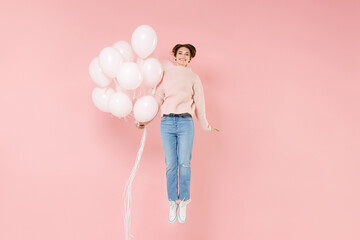 Full length portrait of smiling young woman in casual sweater isolated on pastel pink wall background. Birthday holiday party people emotions concept. Celebrating hold air balloons jumping having fun.