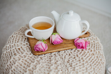 A mug of hot tea, a teapot, a wooden stand on an ottoman. Cozy autumn. Winter breakfast. Roses.