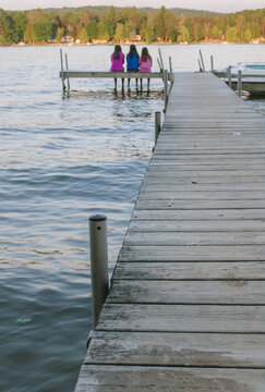 three young women sit at the end of a dock