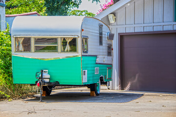 Turquoise and white vintage camper trailer parked beside garage door