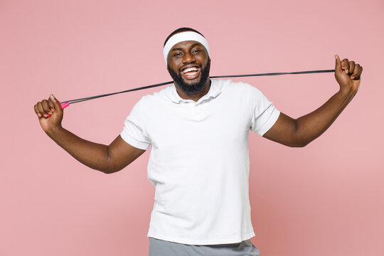 Cheerful young bearded african american fitness sports man in white headband t-shirt hold skipping rope looking camera spending time in gym isolated on pastel pink color background studio portrait.