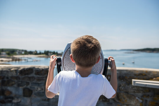 Boy looks through a tourist viewfinder at a scenic waterfront destination