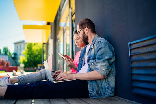 Skilled IT professionals checking notification for cellphone device while creating program code for updating mobile application, millennial colleagues collaborating on web design connected to 4g