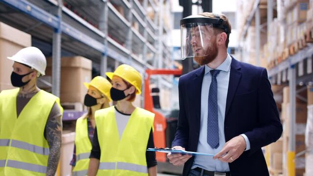 Man manager and workers with face mask walking in warehouse, talking.