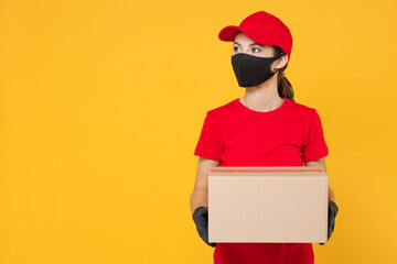 Delivery employee woman in red cap blank t-shirt uniform protect face mask gloves work courier in service during quarantine coronavirus covid-19 virus hold cardboard box isolated on yellow background.