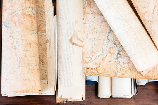 Pieces of an antique map and scrolls sit on a wooden table.