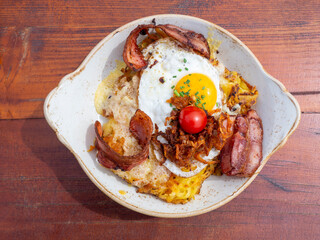 Delicious traditional German mountain dish with cut grilled potatoes, bacon, eggs and melted cheese. View from the top. Dish on a wood table