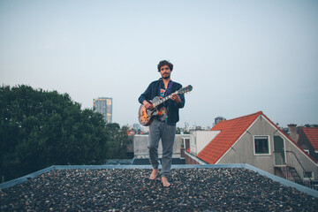 Creative musician playing guitar outside on a rooftop of a building.