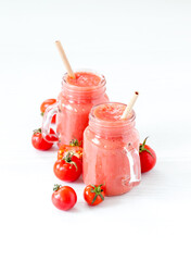 Red tomato smoothie in a glass jar with a bamboo straw on a light background