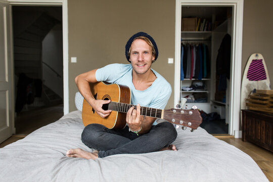 Young man sitting on his bed playing guitar, relaxing