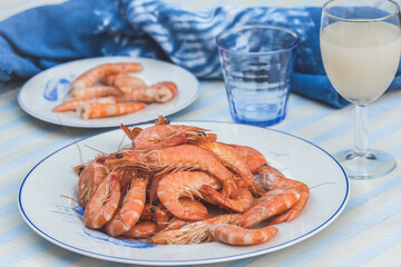 Plate with prawns on a blue and white table and background, smaller plate with peeled prawns in the background