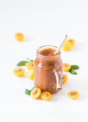 Yellow plum smoothie in a glass jar with a bamboo straw on a light background