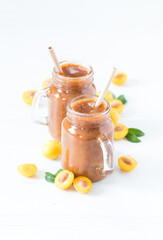 Yellow plum smoothie in a glass jar with a bamboo straw on a light background