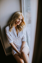 Young blond woman sitting by window at day light