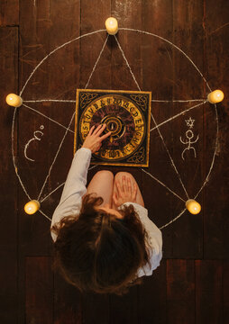 Woman sitting inside a pentagram using a Ouija board.