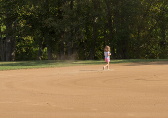 Small toddler girl playing in the sand and dirt of an empty baseball field in the infield area