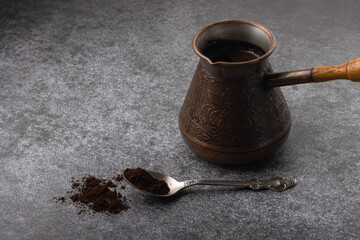 Vintage cezve with brewed coffee and a spoon with ground coffee on grey background