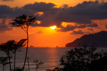 Fototapeta na wymiar Sun behind clouds setting over the Pacific Ocean at Carate Costa Rica