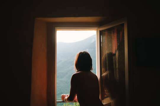 Woman standing at an open window watching the sunrise