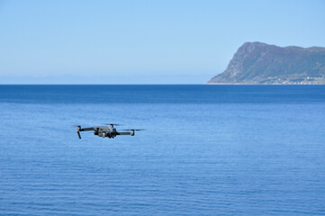 Drone flying in the air, with the sea and mountains in the background.
