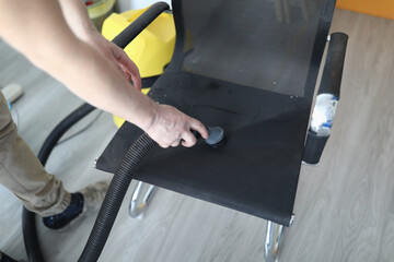 Male hand hold hose with brush from vacuum cleaner. Man clean dust from chair using electrical...