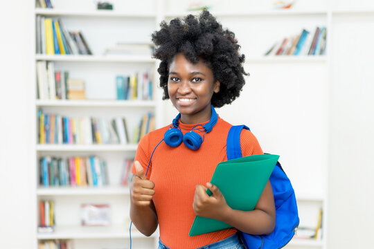 Afro american female college student with backpack and paperwork showing thumb up