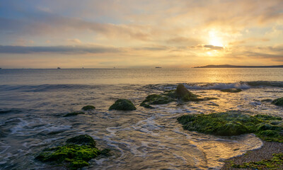 Foaming wave, breaking at sunrise with a rocky shoreline