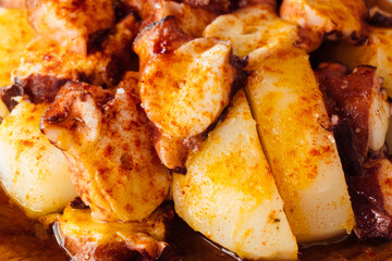 Galician octopus with potatoes in a dark wooden dish. Typical Spanish dish from Galicia.