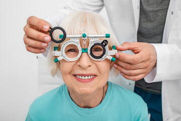 Smiling senior woman wearing optometrist trial frame at ophthalmology clinic. Ophthalmologist...