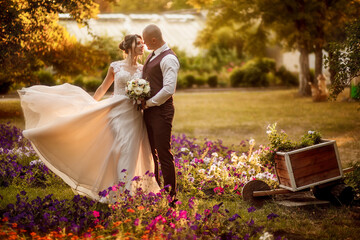 Bride and groom stand in a beautiful green garden on a warm autumn day. Newlyweds walk along the...