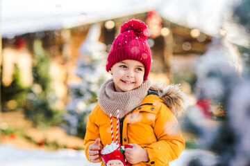 Young boy holding Santa's cup of cacao with marshmallows standing on a fake ice rink.
