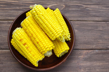 Young sweet tasty grilled corn in a clay plate on a wooden dark background. Summer food.