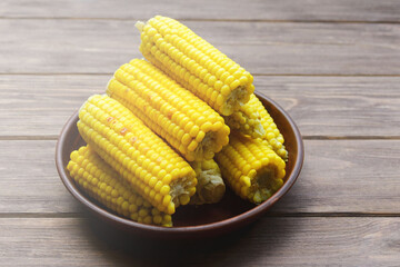 Young sweet tasty grilled corn in a clay plate on a wooden dark background. Summer food.