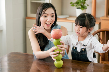 Asian mother and daughter play by set apples together on table in the kitchen. Concept of enjoy with family time of different age of member in their house.