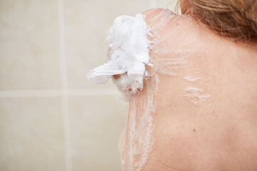 an elderly 60-year-old woman washes in the shower, Soaps her shoulders, back and body with a washcloth in the home bathroom