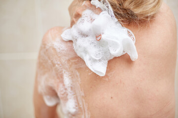 an elderly 60-year-old woman washes in the shower, Soaps her shoulders, back and body with a washcloth in the home bathroom