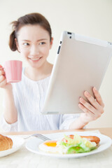 Obraz na płótnie Canvas タブレットPCを見ながら朝食を食べる女性