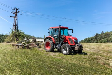 Red tractor working in a field with a two-rotor tedder. Drying hay in the meadow. Work on an...