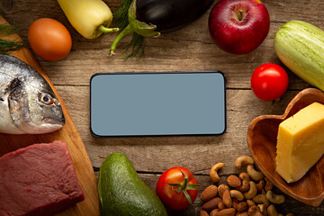 Keto diet inscription and food and smartphone . Healthy products. Diet concept low carbs. Vegetables, fish, meat, nuts, seeds, tomato, apple, cheese on a brown background. Top view.