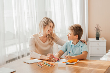 smiling mother helping adorable son doing schoolwork at home