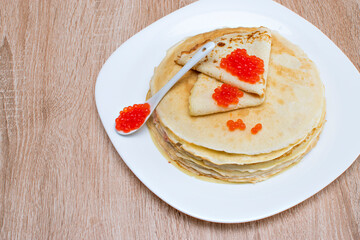 Pancakes with red caviar. Pancakes with caviar on a white plate. Pancakes with red caviar on a plate and a wooden board.