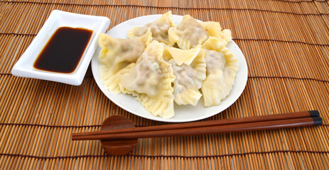 wontons on a plate over a bamboo mat, with chopsticks and dipping sauce. Selective focus and deliberate shallow depth of field for effect.