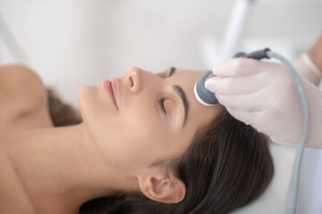 Young woman lying down with eyes closed during professional beauty procedures