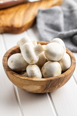 Fresh white champignon mushrooms in wooden bowl.