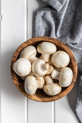 Fresh white champignon mushrooms in wooden bowl.