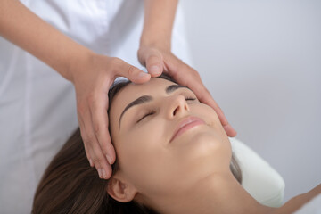 Professional massage therapist massaging forehead of customer