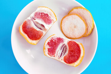 Two halves of sliced grapefruit on white plate on blue background. Diet concept, top view