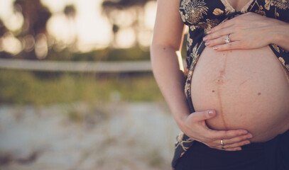 pregnant woman holding her belly on the beach outside 