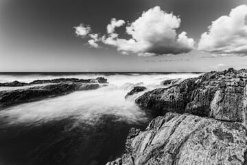 Une longue exposition dramatique en noir et blanc de la côte rocheuse en Espagne pendant une journée lumineuse et nuageuse