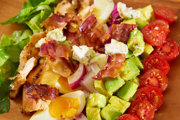 Fresh salad of chicken, avocado, corn, onions, eggs and bacon closeup in a plate on the table